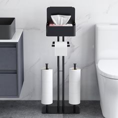 a white toilet sitting next to a black and white stand with two rolls of toilet paper