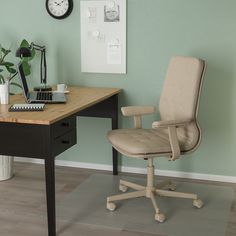 a desk with a chair, clock and plant on it in front of a green wall