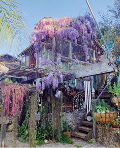 a house with purple flowers growing on the roof and stairs leading up to it's second story