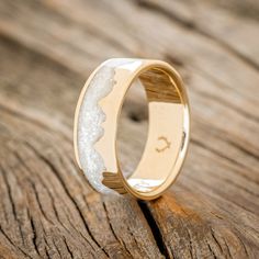 a wedding ring with white and gold inlays on top of a wooden surface