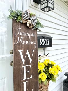 a welcome sign on the front door of a house with yellow flowers and greenery