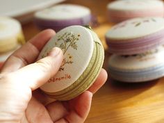 a person is holding a small round box with flowers on it and four cookies in the background