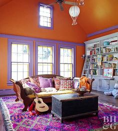 a living room with an orange wall and purple trim on the ceiling is filled with bookshelves