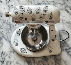 a kitchen aid mixer with cupcakes on it's side sitting on a marble counter top