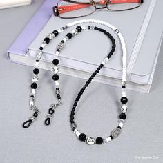 Tired of misplacing your reading glasses? Our black and white eyeglass chain offers you a stylish and secure solution to this problem. Ideal gift for those who are like me and are forever misplacing their eyeglasses. Rubber loops adjust to fit most glasses frames.   🦉Product Details:  * Approx. Length - 32 in (including rubber loops) * Chain Weight: 1.3 oz * Bead Color(s): Black, White * Metal Color: Silver-tone * Material: Glass and Ceramic Beads, Metal Beads, Czech Beads * Closure: Lobster Claw Clasps and Rubber Loop Ends * Product ID: G206 🎁 Gift packaging available at Checkout ($4.00 USD) - See last image   🦉NOTES: * Not recommended for young children! * The lobster clasps make replacement of the rubber loops easy if they break. * All measurements and weights are approximate and may Adjustable Black Beads Glasses Chains As Gift, Handmade Black Glass Glasses Chains, Adjustable Beaded Black Glasses Chains, Black Metal Glasses Chain With Adjustable Length, Black Metal Adjustable Glasses Chain, Beaded Eyeglass Chain, Glasses Chains, Chain Loop, Owl Jewelry