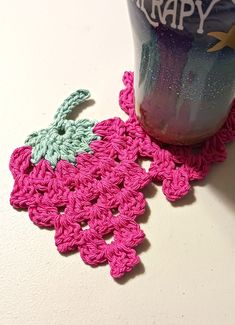 a pink crocheted doily next to a cup on a white counter top