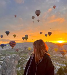 a woman standing on top of a hill looking at hot air balloons in the sky