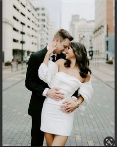 a man and woman standing next to each other on a brick road in front of tall buildings