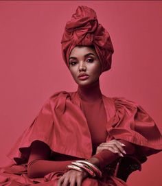 a woman in a red dress and head wrap sitting on a pink chair with her hands on her knees