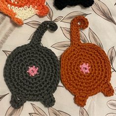 three crocheted items are sitting on a tablecloth, one has a black cat and the other is an orange cat