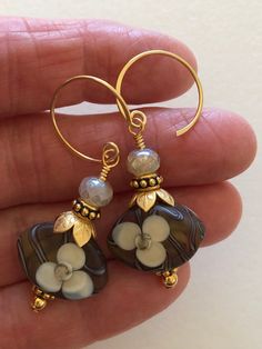 "Beautiful artisan lampwork bead earrings with hand painted white flower motif in light brown, amber, and white accented with leafy gold bead caps on 24k gold vermeil ear wires. The gorgeous translucent lampwork beads are 12 x 18 x 7mm ovals with smooth matte finish and raised floral design. Slivers of glass and fine silver are used to \"draw\" the intricate designs then beads are kiln fired at +900 degrees. The result is a unique one of a kind lampwork bead. Lovely flower beads are topped with Glass Flower Earrings, Lampwork Bead Earrings, Lampwork Earring, Aquamarine Earrings, Earring Designs, Jewelry Designers, Flower Motif, Flower Beads, Handmade Copper