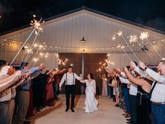 the bride and groom are walking down the aisle with sparklers in their hands as they exit the barn