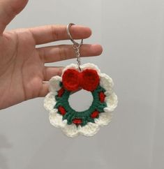 a hand holding a crocheted christmas wreath ornament with a red bow