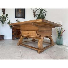 a large wooden table sitting on top of a tile floor next to a potted plant