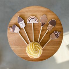 some cupcakes are sitting on top of a wooden plate with paper cutouts in the shape of houses and clouds