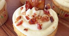 several cupcakes with white frosting and bacon toppings on top, sitting on a wooden table