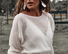 a woman wearing a white sweater and black pants is standing in front of a fence