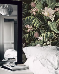 a mirror sitting on top of a bed next to a wallpaper covered in flowers