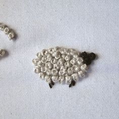 two sheep made out of beads sitting on top of a white cloth covered tablecloth