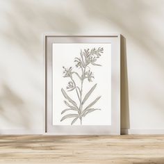 a white framed art print sitting on top of a wooden table next to a plant