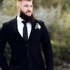 a man with a beard wearing a suit and flower in his lapel is looking at the camera