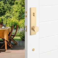 an open door with a table and chairs in the yard next to some trees, shrubs and bushes