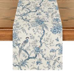 a blue and white floral table runner with birds on the top, in front of a wooden table