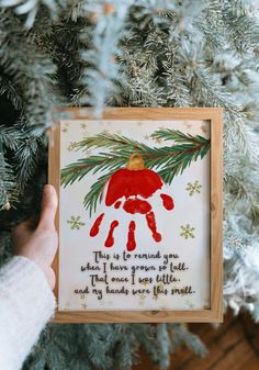 a handprinted christmas ornament hanging on a tree with someone holding it