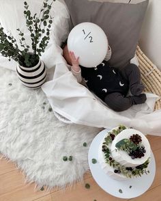 a baby holding a balloon while sitting in a chair next to a cake and potted plant