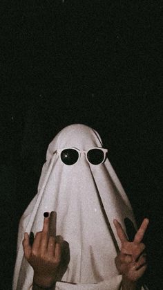 a person wearing sunglasses and a ghost mask making the peace sign with their hands in front of them