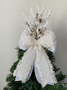 a christmas tree decorated with white and silver decorations on top of green leaves, branches and balls