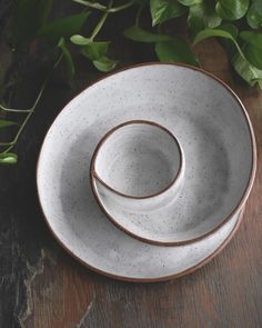 two white and brown dishes sitting on top of a wooden table next to green leaves