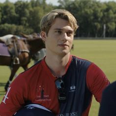 a man in a red shirt standing next to another man with a horse behind him