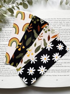 four bookmarks on top of an open book with flowers and rainbows in the background