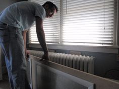 a man standing on top of a radiator next to a window with blinds