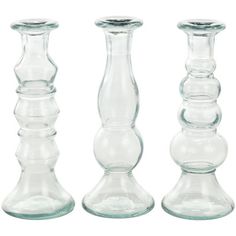 three clear glass candlesticks are lined up on a white background with one candle holder in the middle