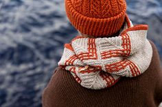 a person wearing an orange hat and scarf looking out at the ocean from behind them