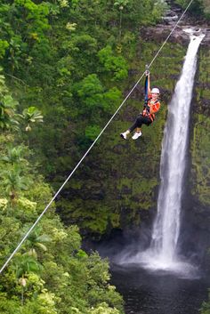 a man is high in the air above a waterfall while zipping through the trees