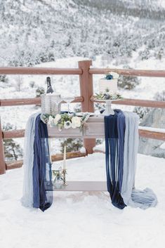 Dive into this dreamy Mount Charleston wedding setup! A rustic wooden table, adorned with a two-tiered wedding cake featuring wildflower charm, stands beautifully amid a snowy forest. Flowing blue fabrics and elegant centerpieces set the perfect fall wedding scene. 🍰🌲❄️ #fallwedding #weddingideas #weddingcakes #winterwedding #wildflowerweddingtheme Snowy Desert, Vegas Wedding Reception, Small Private Wedding, Destination Wedding Reception, Snowy Wedding, Dream Wedding Reception, Pretty Wedding Cakes, Romantic Wedding Receptions, Intimate Wedding Reception