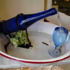 a blue bottle pouring water into a white bowl filled with green plants and dirt in it