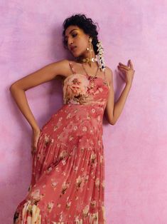 a woman in a pink dress leaning against a wall with her hand on her hip