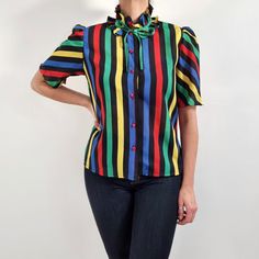 Beautiful vintage blouse in black, blue, red, green and yellow stripes with a frilly collar. It has a simple, straight shape, puffed short sleeves, collar ties and six, red buttons fastening. It is made from lightweight, slightly see-through fabric. Perfect, cheerful blouse for everyday or special occasions. No brand label. 100% polyester. No size label, would fit Small to Medium sizes. Measurements when laid flat are: Pit to pit: 50cm Waist: 80cm Shoulders length: 38cm Length: 60cm. Great condition, apart from one pulled thread on the front. Please see photo. B. Multicolor Collared Shirt For Work, Fitted Multicolor Puff Sleeve Blouse, Multicolor Fitted Blouse With Puff Sleeves, Striped Short Sleeve Blouse With Ruffles, Multicolor Short Sleeve Work Shirt, Multicolor Collar Blouse For Work, Retro Short Sleeve Blouse For Work, Fitted Striped Blouse With Ruffles, Multicolor Short Sleeve Top With Striped Collar