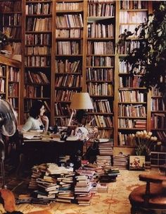 a woman sitting at a desk in front of a bookshelf filled with lots of books