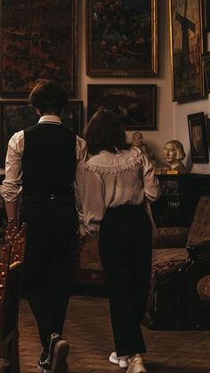 two people are standing in front of paintings and looking at each other's back