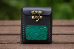 a small black and green leather case with brass hardwares on the front, sitting on a wooden surface