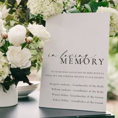 a memorial card sitting on top of a table next to white flowers and greenery