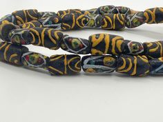 Antique Venetian Black African Trade Beads with beautiful Ethnic African Pattern design in yellow, light blue, white, red, and green.  The beads are handmade, each bead is unique, and they are rare. There are a few imperfections throughout the beads due to the fact they're handmade and old. Sizes, conformity and colors vary.  You will receive the strand shown in the pictures. The strand is about 68cm/27" long. Bead sizes vary.  If you have additional questions about this item, please don't hesit Artisan Yellow Beads For Festivals, Artisan Yellow Wooden Beads, Traditional Yellow Beads For Festivals, Large Yellow Beads For Festivals, Traditional Large Yellow Beads, Artisan Yellow Beaded Necklaces For Festivals, Yellow Large Beads For Festivals, Unique Hand-strung Yellow Beads, Traditional Yellow Beaded Necklaces With Polished Beads