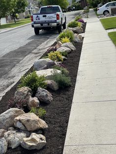 a truck parked on the side of a road next to some rocks and flowers in front of a house