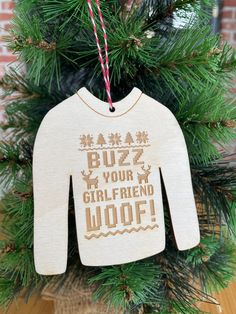 a sweater ornament hanging from a christmas tree with the words buzz your girlfriend woof on it