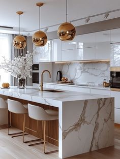 a kitchen with marble counter tops and gold pendant lights hanging from the ceiling over the island